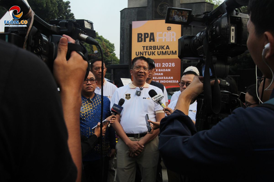 Man in a white polo speaks to reporters as cameras and microphones surround him at a BPA Fair press event outdoors.