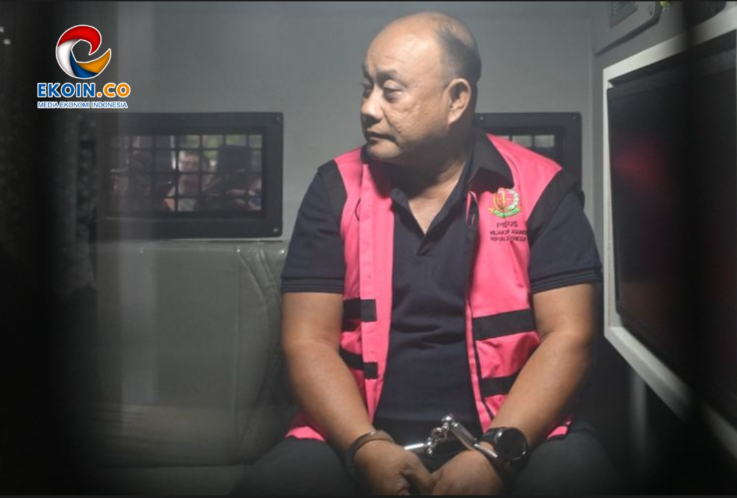 Man in a pink safety vest sits in a vehicle, looking to the side, with a logo 'EKOIN.CO' visible in the top-left corner.