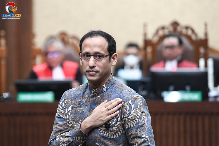 Man in a patterned shirt places his right hand over his heart during a formal oath as officials sit behind him in a court or council chamber.