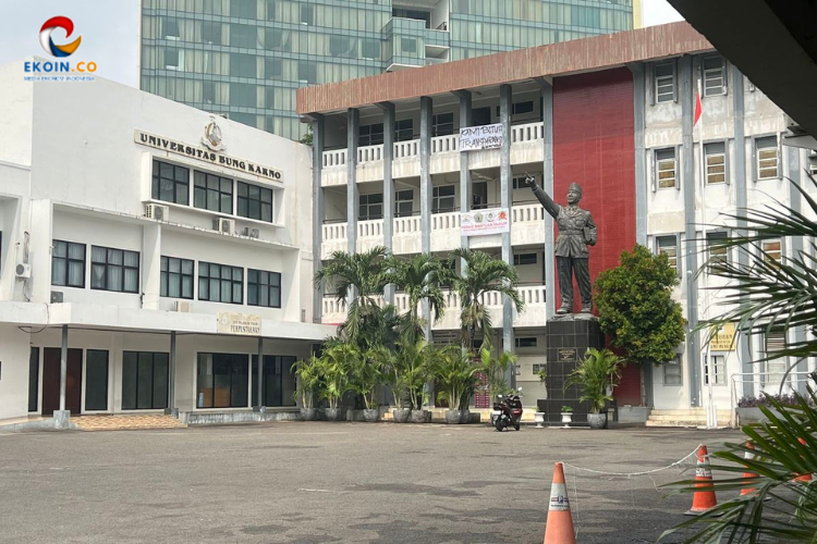 Front view of Universitas Bung Karno campus building with a tall statue in the plaza and palm trees in front.