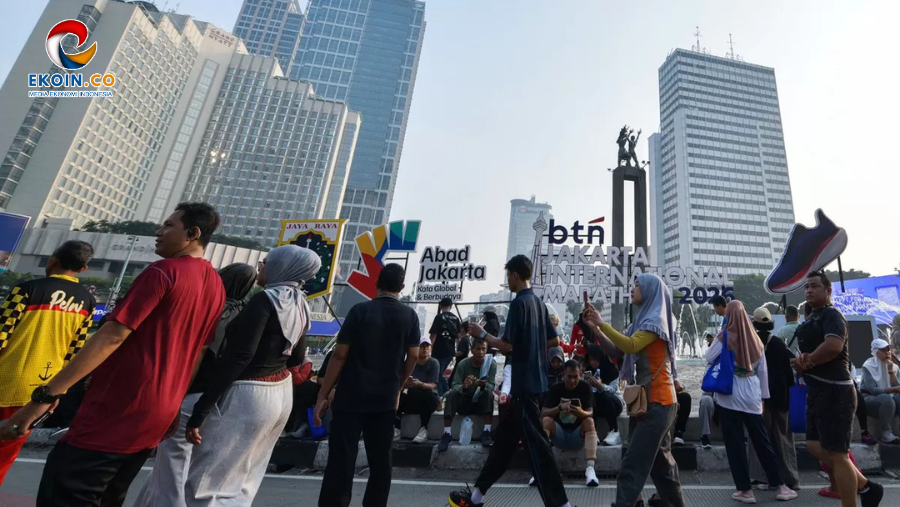 Crowd of people gathered on a city street with tall buildings and event signage for a Jakarta marathon, logo visible in corner.