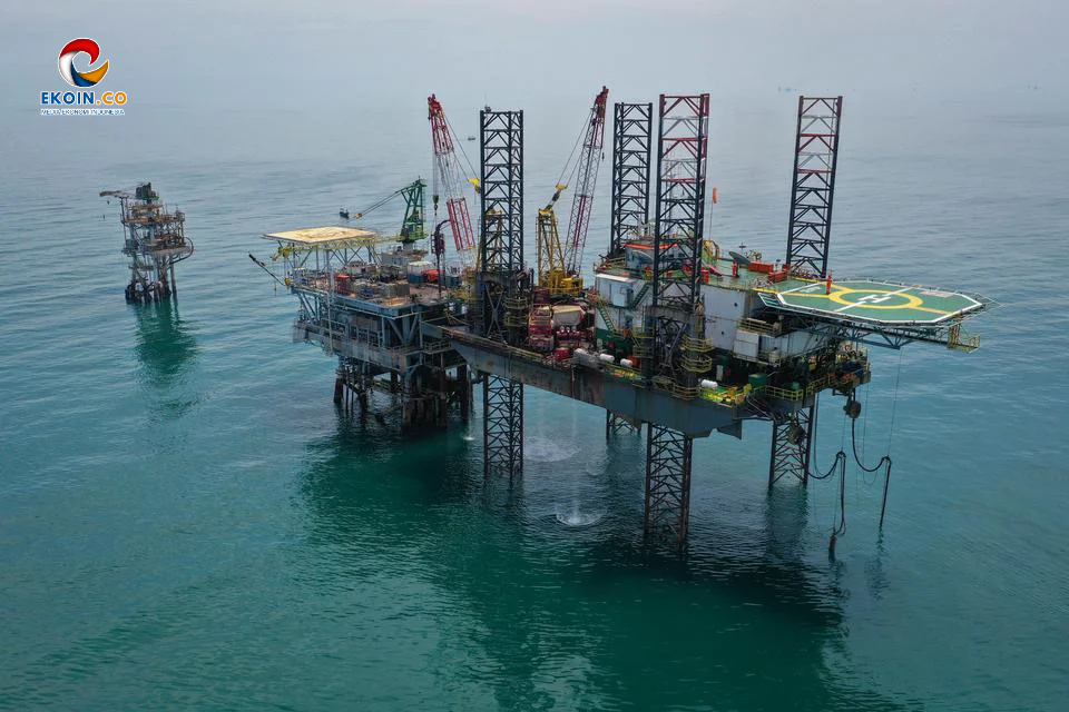 Offshore oil platform with cranes and a helipad, standing on stilts above teal sea; logo in the corner.