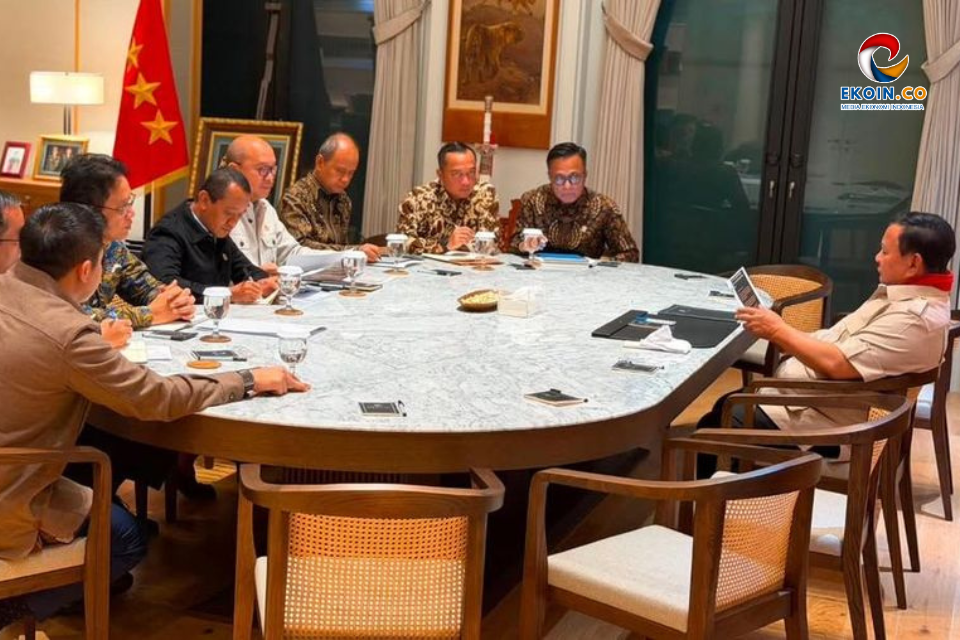 Group of officials seated around a large marble conference table in a formal meeting room, Indonesian flag in background, Ekoin logo top right.