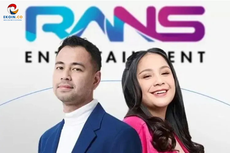 Two smiling hosts, a man in a blue suit and a woman in pink, pose in front of a Trans Entertainment backdrop.