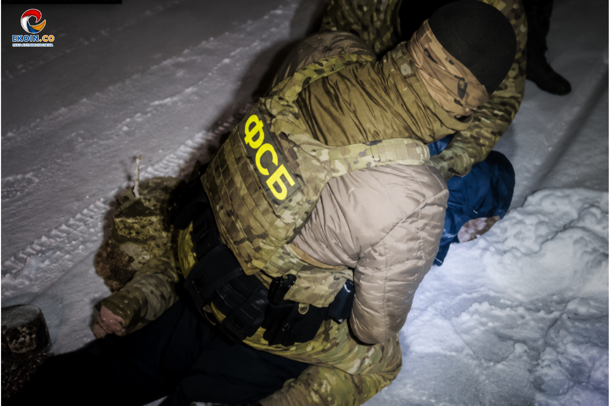 Soldiers in camouflage armor assist a person lying in the snow during a night operation, one with a labeled tactical vest reading OC05; scene on a snowy street corner.
