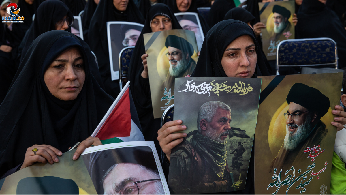 Group of women wearing black hijabs at a demonstration, holding posters with portraits and a small Palestinian flag visible among them.